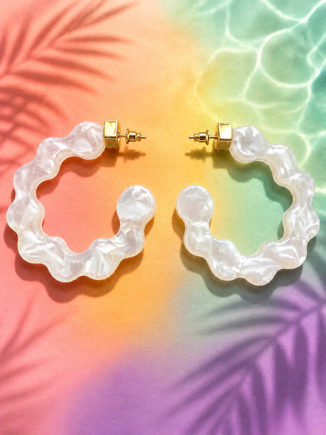 sculptural statement hoop earrings made of glossy marbled white resin with soft pearl-like swirls and gold-tone stud posts,