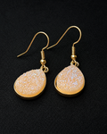 Gold earrings with beige stone-like designs on a black background