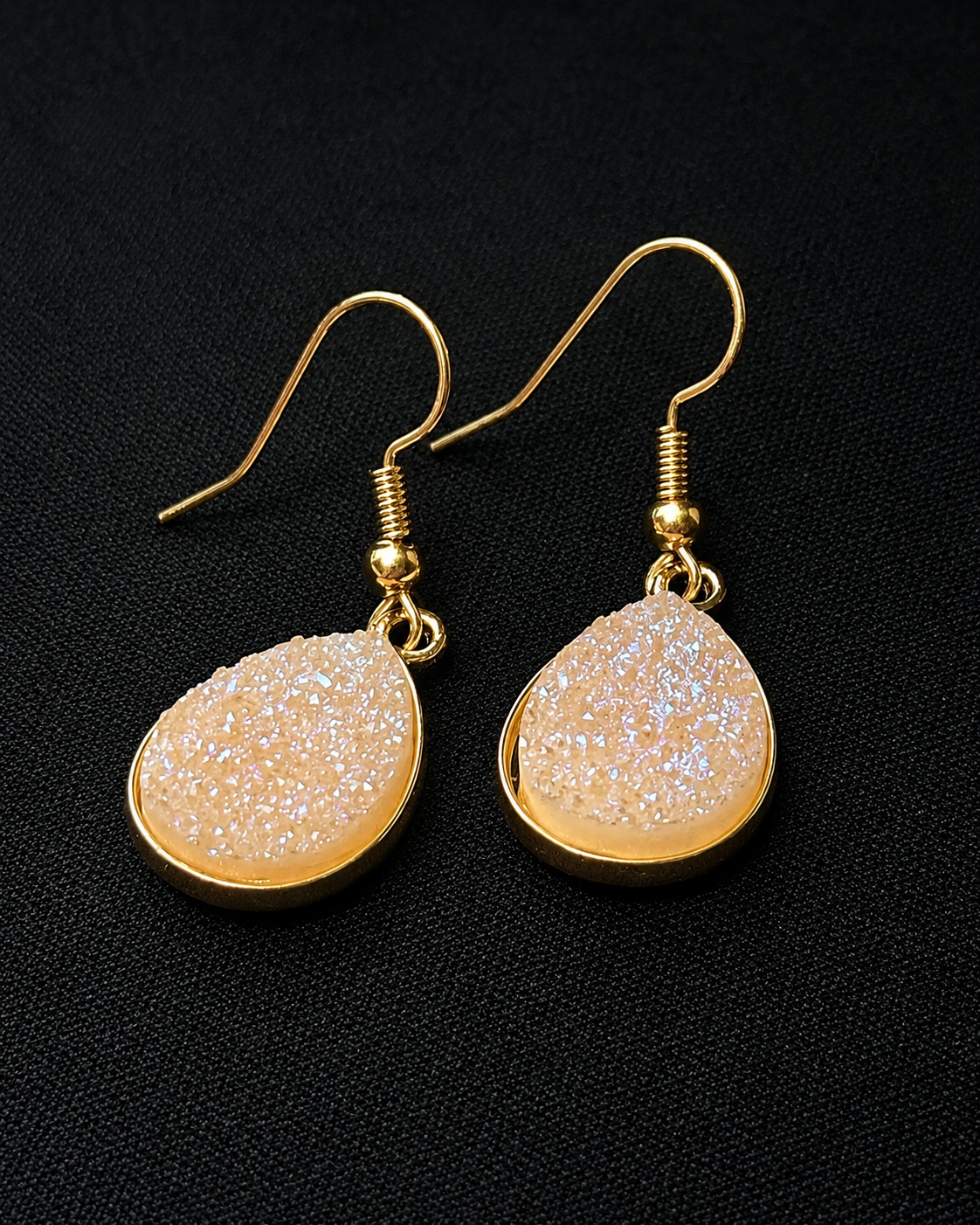Gold earrings with beige stone-like designs on a black background