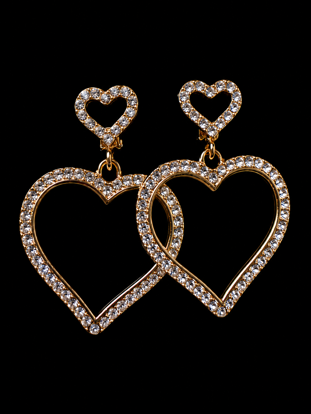 Heart-shaped earrings with gold frame and clear stones on a black background