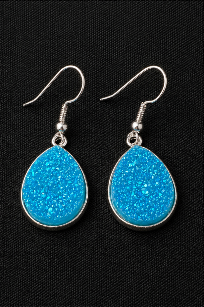 Teardrop-shaped blue earrings with silver hooks on a black background